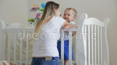 可爱的蹒跚学步的男孩笑着被婴儿床上的母亲挠痒痒